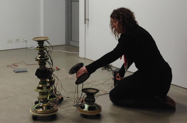 Charlotte kneels on the floor stacking speaker cones on top of each other.