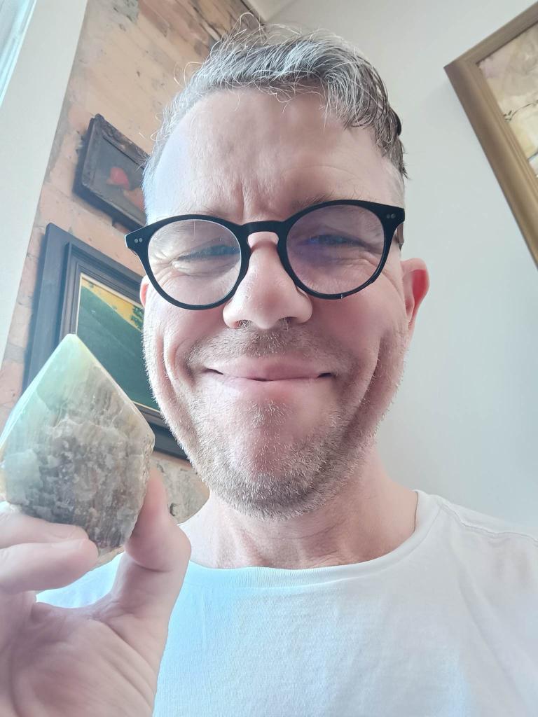 Chris smiles. His glasses are thick and dirty. He holds a crystal with pride