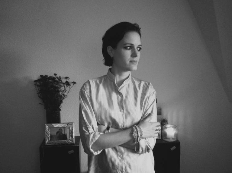 Gemma Thompson stands with her arms loosely folded. She is in thought