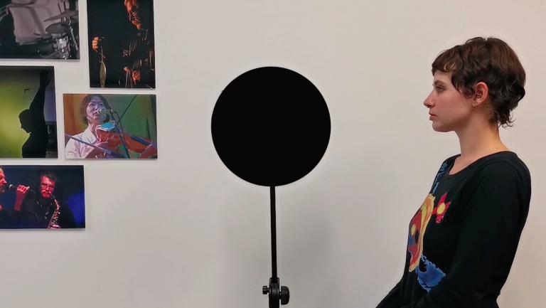 a black circle on a stand. A person stands next to it in profile