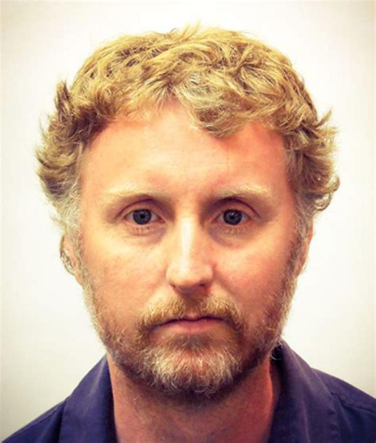 A stark headshot of Mark. He is in front of white wall. This could well be a passport photo.