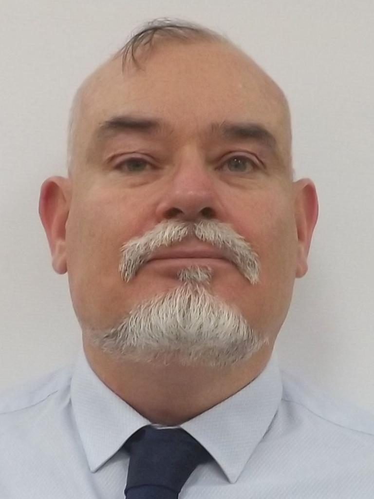 a portrait of Sam. He is looking directly at the camera with a strong and clear face. He has a well groomed goaty and moustache. He is wearing a shirt and tie.