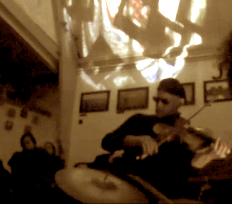 a very blurred photo of Peter playing viola. He is wearing dark sunglasses and a beret. There is a play of light on the ceiling.