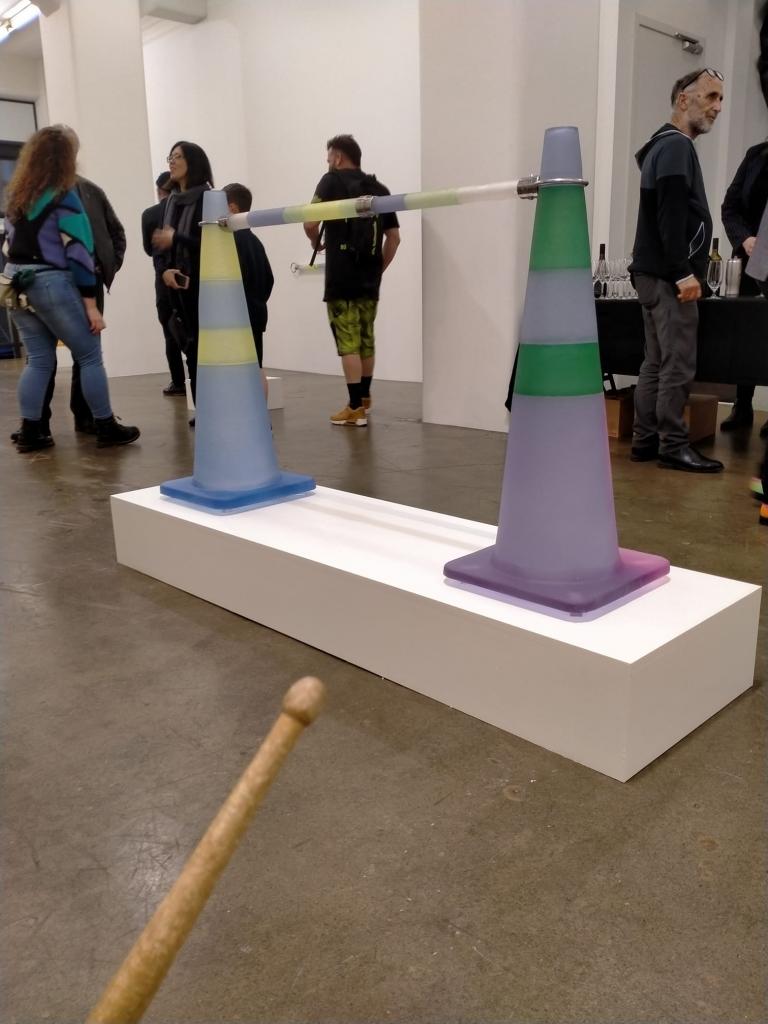 an image from a first person perspective; you are holding a drum stick and advancing towards two lilac coloured roadcones. You are in an art gallery
