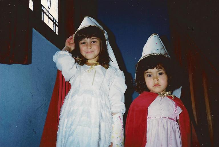 Heleyni and Marika as children. They are dressed in princess outfits with tall hats. Marika looks reserved and Heleyni is smiling
