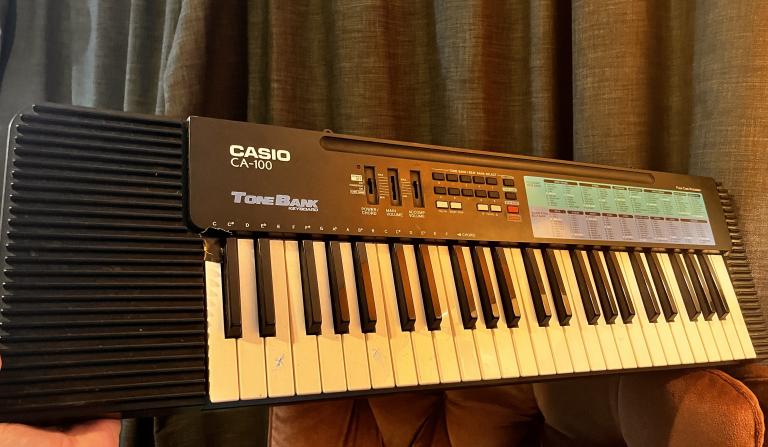 An actual casio CA-100. It is resting on a chair back and has clearly been lit by a lamp out of shot. There is gaffer tape stuck to one of the keys.