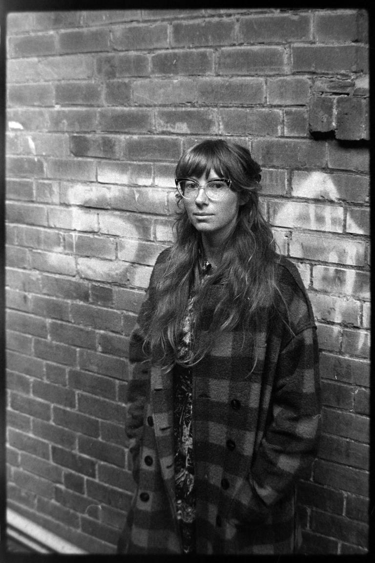 a person in a checkered coat leaning against a brick wall