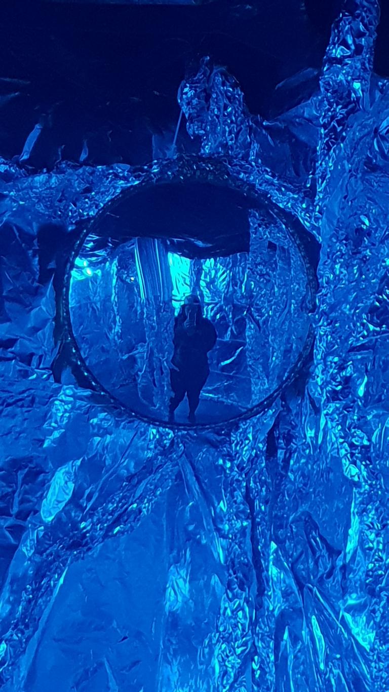 Marika in a fish eye mirror surrounded by tinfoil, all in a blue light